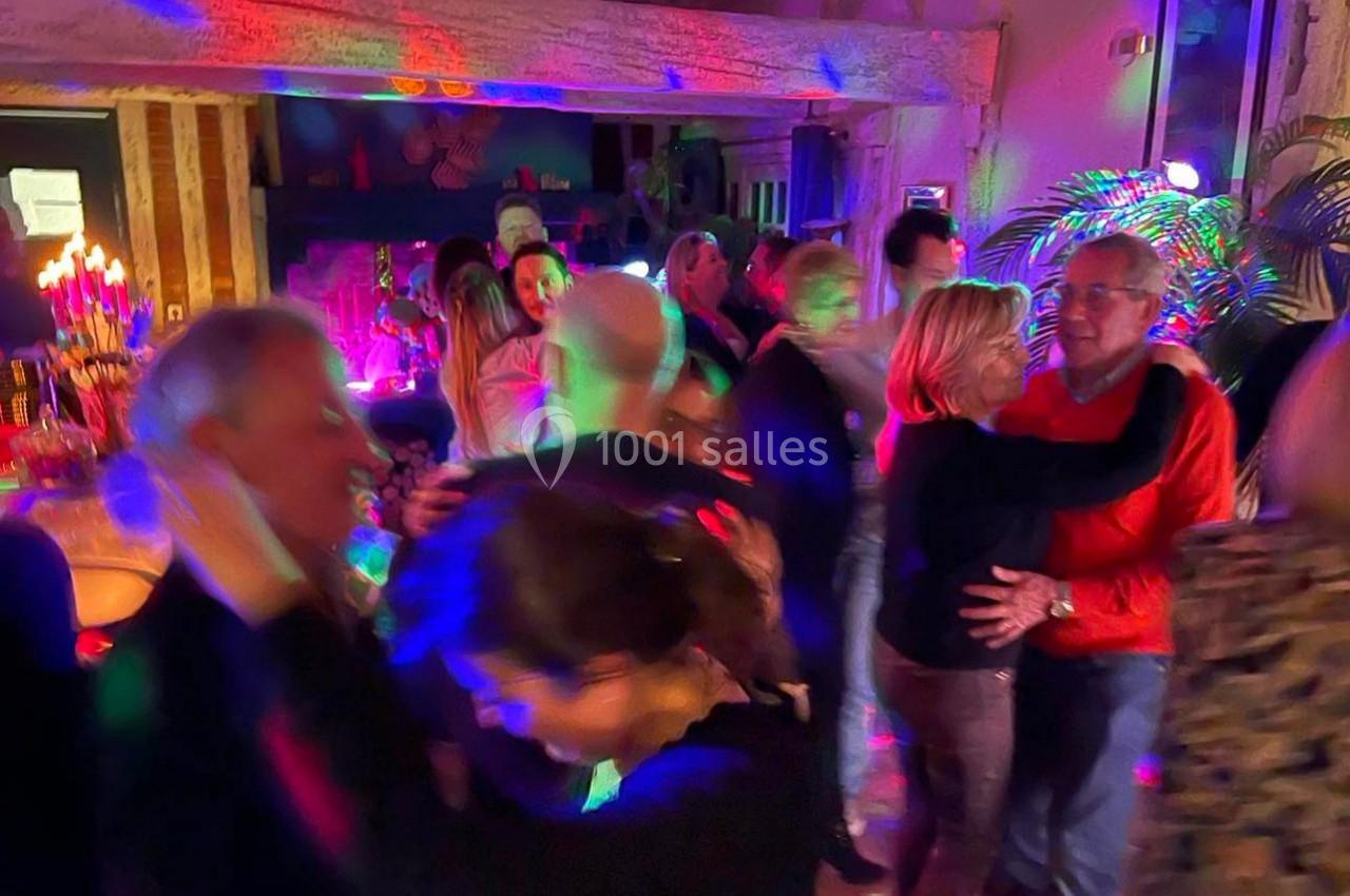 Des personnes dansent dans une ambiance festive avec éclairages colorés dans une salle chaleureuse.