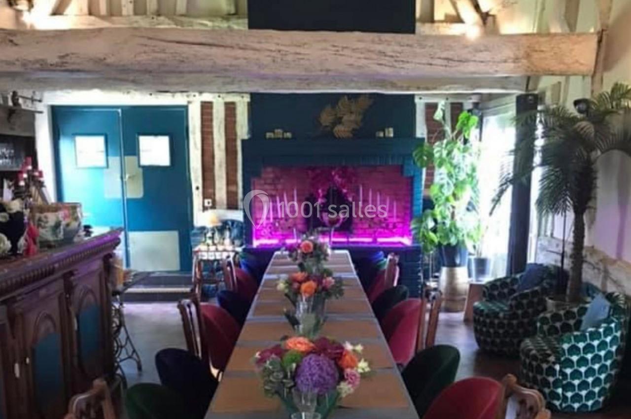 Salle à manger décorée avec une longue table, des chaises colorées, des plantes et une cheminée illuminée.