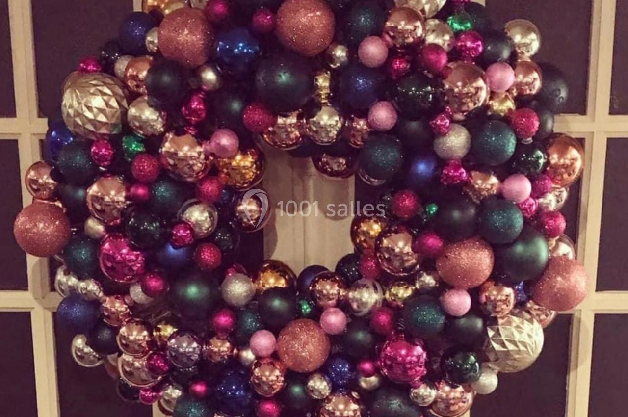 Couronne décorative composée de boules de Noël colorées accrochée sur une porte vitrée.