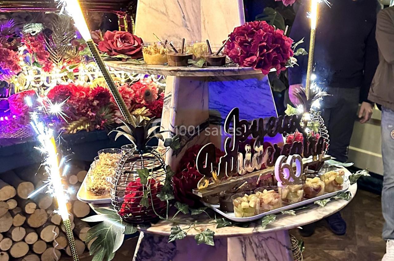 Présentoir décoré avec desserts, fleurs et pancarte ’Joyeux anniversaire 60’ entouré de cierges étincelants.