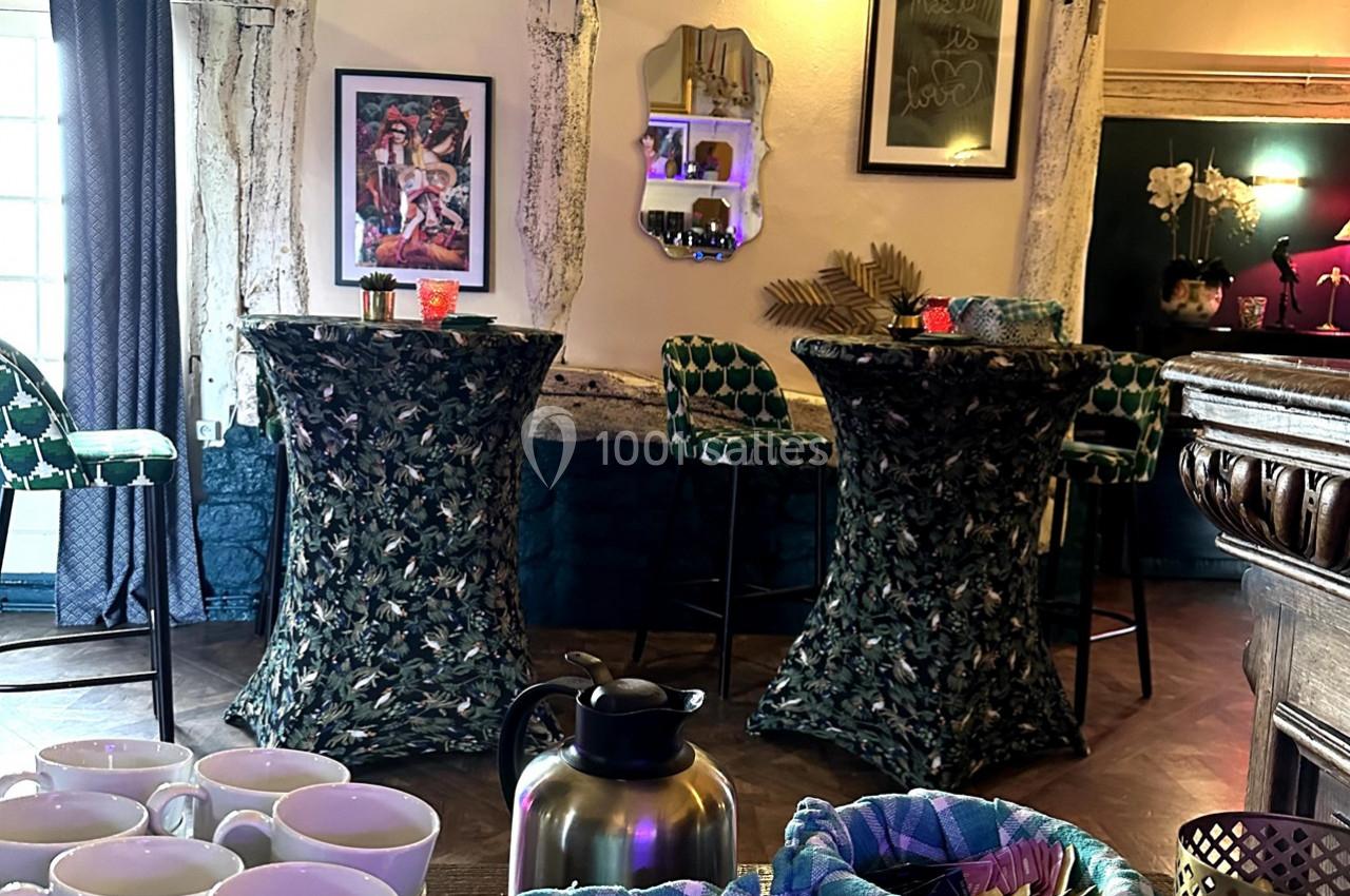 Salle décorée avec des tables hautes recouvertes de nappes à motifs, chaises vertes et éléments muraux colorés.
