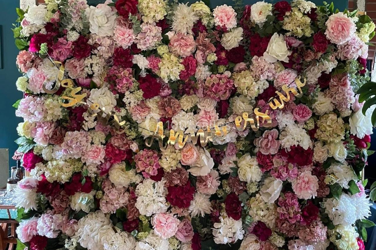 Mur de fleurs multicolores avec une guirlande dorée indiquant ’Joyeux Anniversaire’.