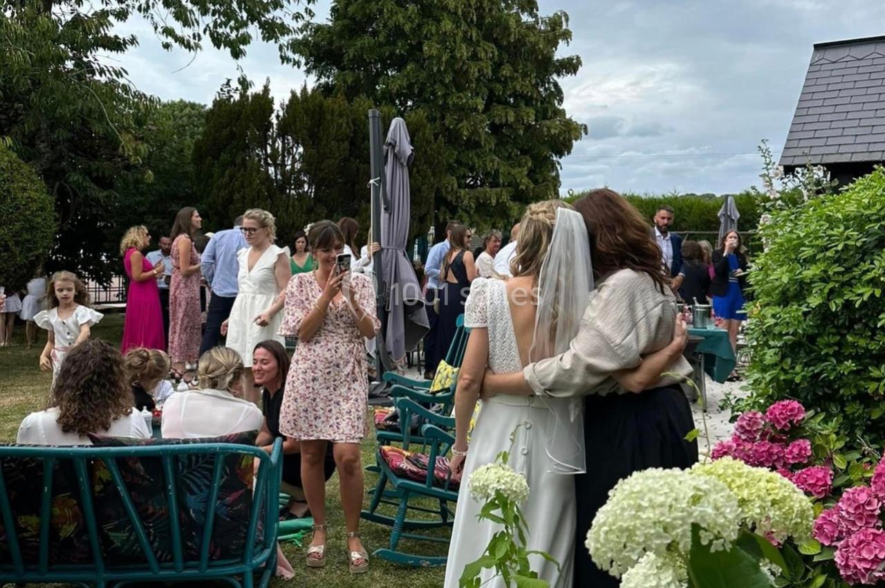 Groupe de personnes réunies dans un jardin, avec une mariée en robe blanche vue de dos.