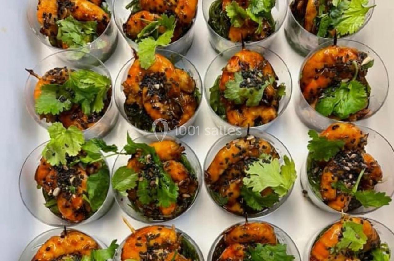 Crevettes marinées servies dans des verrines avec herbes fraîches, graines de sésame et lit de légumes verts.