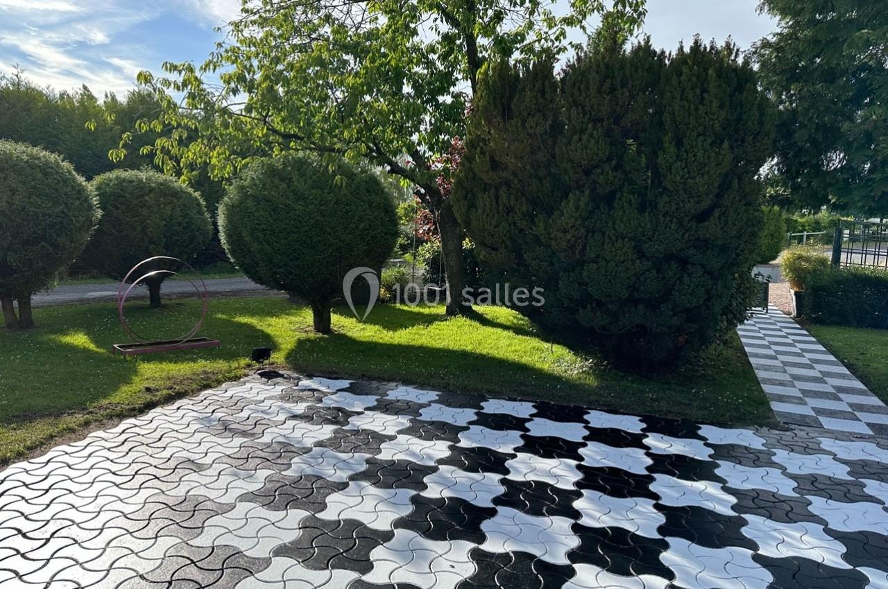 Allée pavée en noir et blanc bordée d'arbres et d'arbustes dans un jardin ensoleillé.