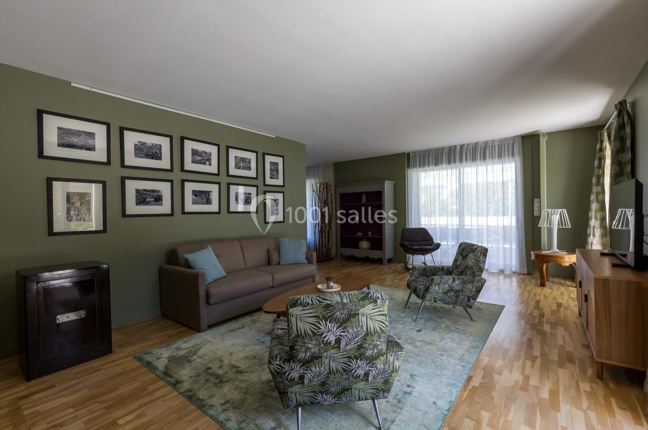 Salon lumineux avec canapé, fauteuils à motifs, tapis, meubles en bois, murs verts et galerie de photos encadrées.