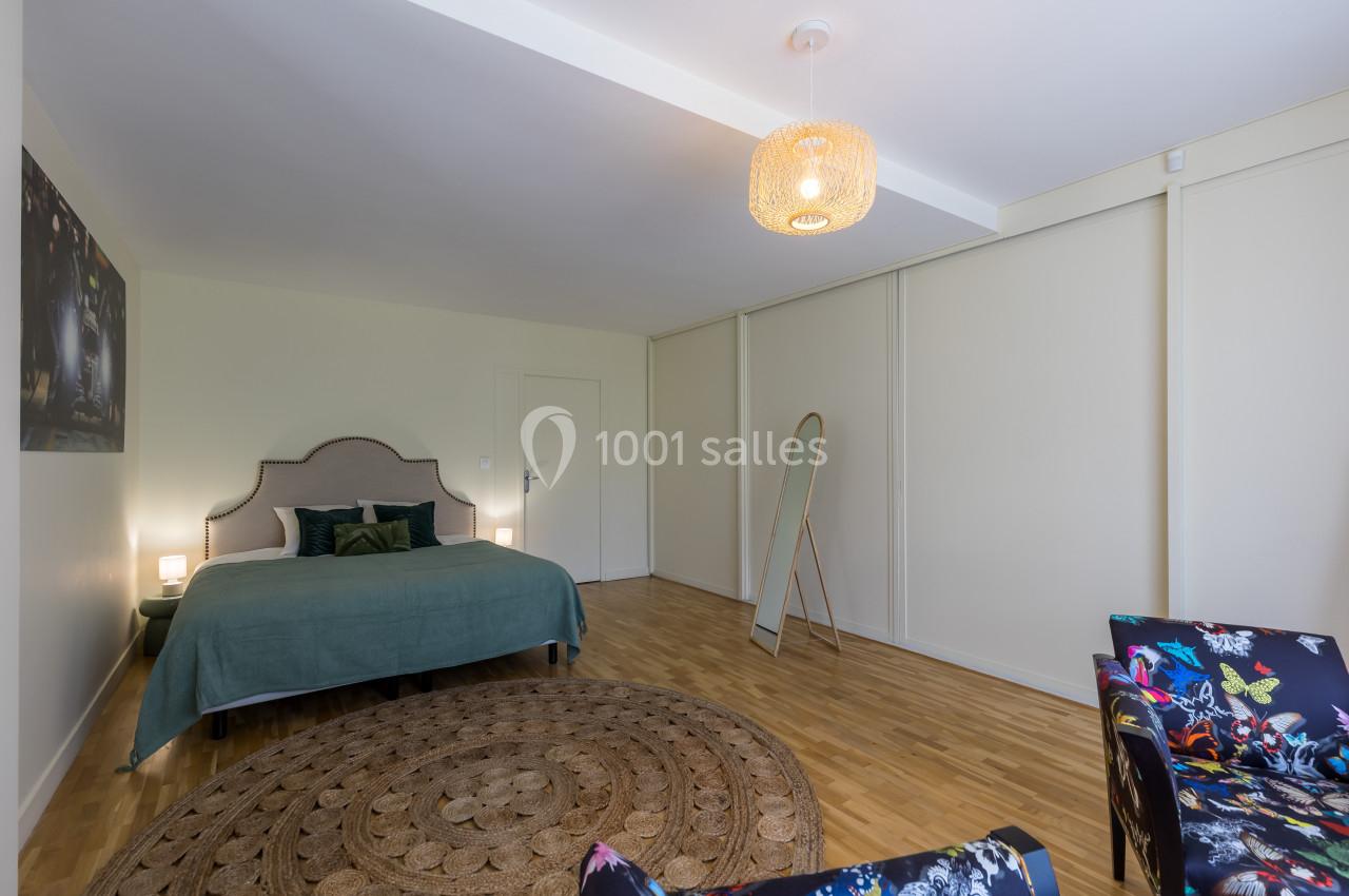 Chambre lumineuse avec lit double, tapis rond, miroir sur pied et fauteuil coloré, sur parquet en bois clair.