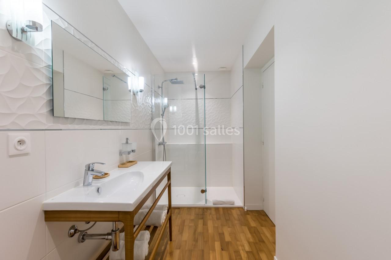 Salle de bain moderne avec douche vitrée, lavabo sur meuble en bois et sol en parquet.