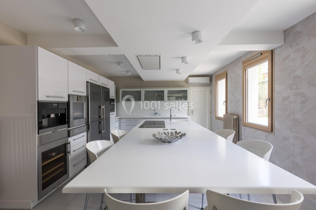 Cuisine moderne avec un grand îlot central blanc, des appareils encastrés et des fenêtres laissant entrer la lumière…