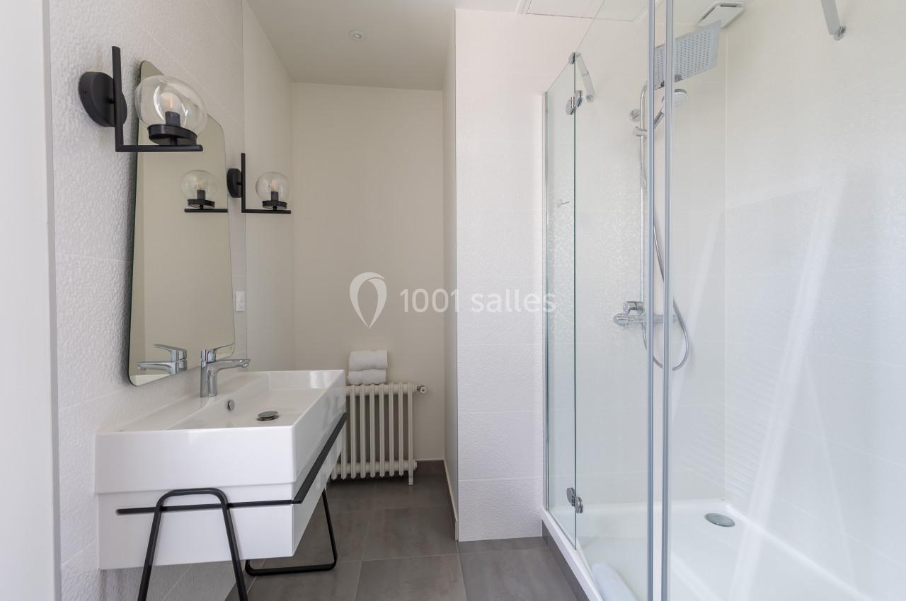 Salle de bain moderne avec lavabo, miroir, douche vitrée et murs blancs.