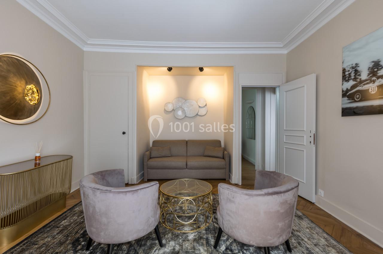 Salon élégant avec canapé gris, deux fauteuils velours, table basse dorée et décoration murale lumineuse.