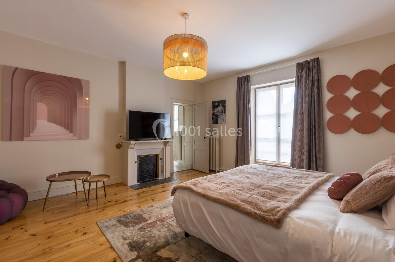 Chambre lumineuse avec lit double, parquet, cheminée, télévision, et décoration murale moderne dans des tons chauds.