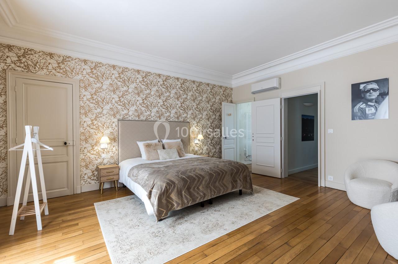 Chambre lumineuse avec lit double, parquet en bois, murs décorés de papier peint floral et mobilier minimaliste.
