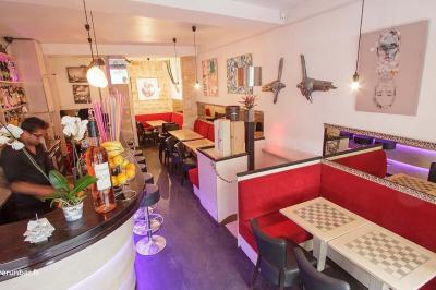 Terrasse animée d'un café avec des clients assis à des tables en plein air, entourée d'arbres et de bâtiments.