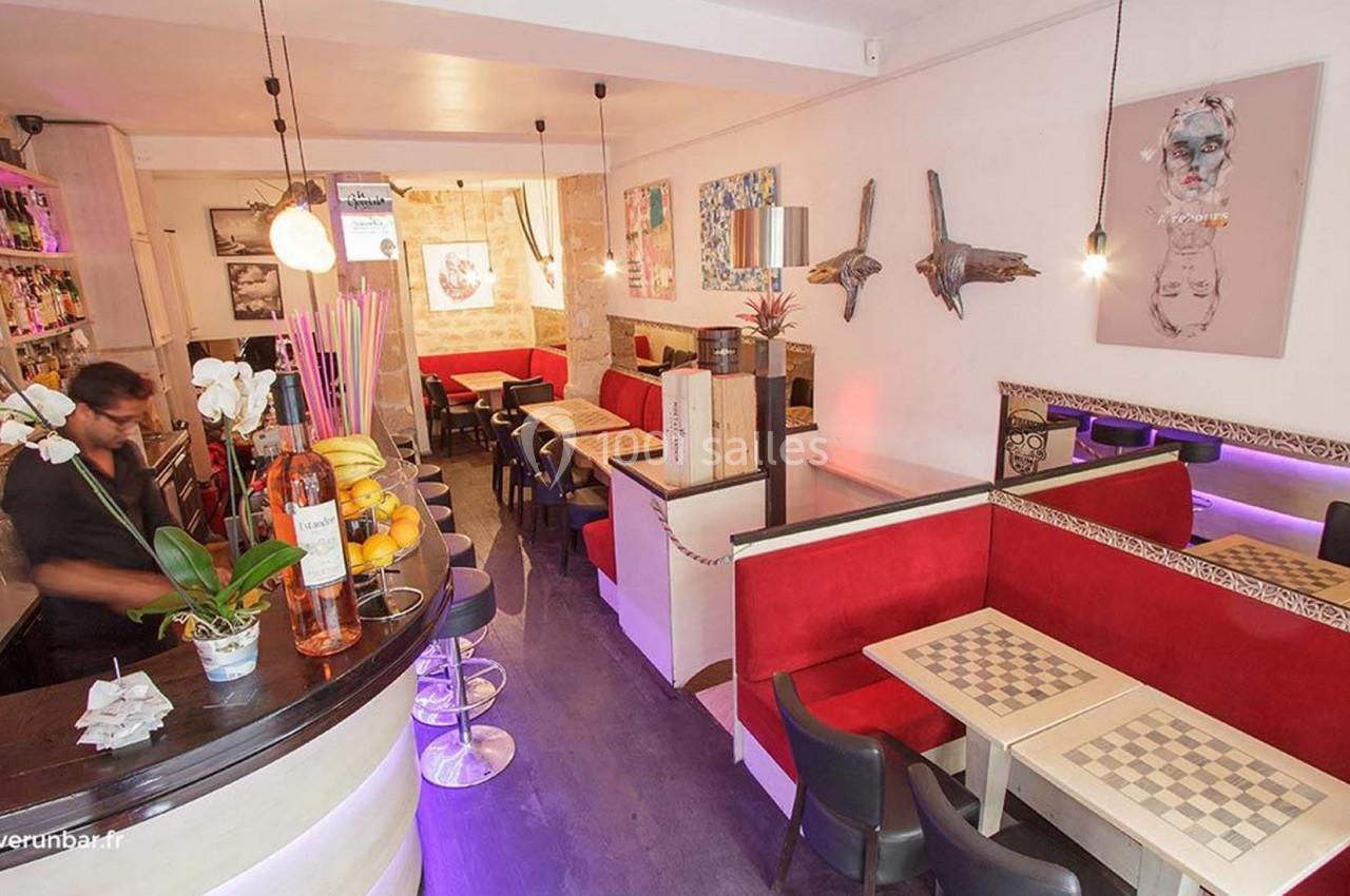 Intérieur d'un bar avec comptoir, tables à damier, banquettes rouges et décorations murales artistiques.