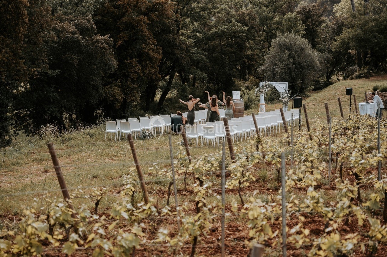 Chaises blanches disposées en extérieur dans un vignoble, avec quelques personnes en train de préparer l'espace.