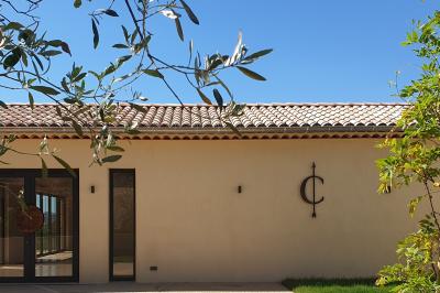 Entrée d'un bâtiment moderne entourée de cyprès et d'oliviers, avec un chemin menant à une porte vitrée.