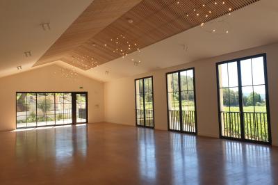 Entrée d'un bâtiment moderne entourée de cyprès et d'oliviers, avec un chemin menant à une porte vitrée.