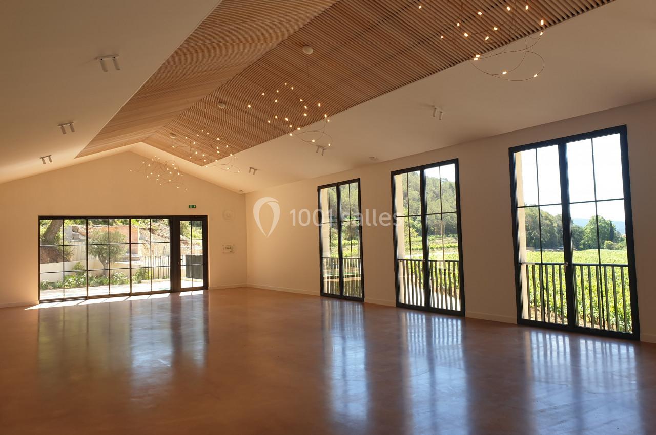 Salle lumineuse avec de grandes baies vitrées, un plafond en bois incliné et des lumières suspendues.