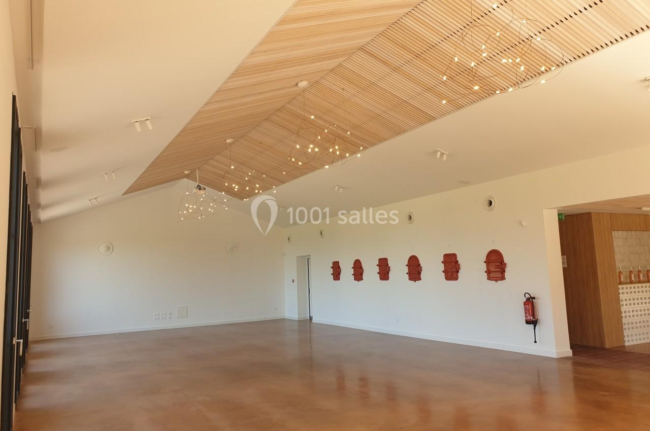 Salle lumineuse avec un plafond en bois, des luminaires suspendus, un mur décoré de motifs rouges et un sol en béton poli.