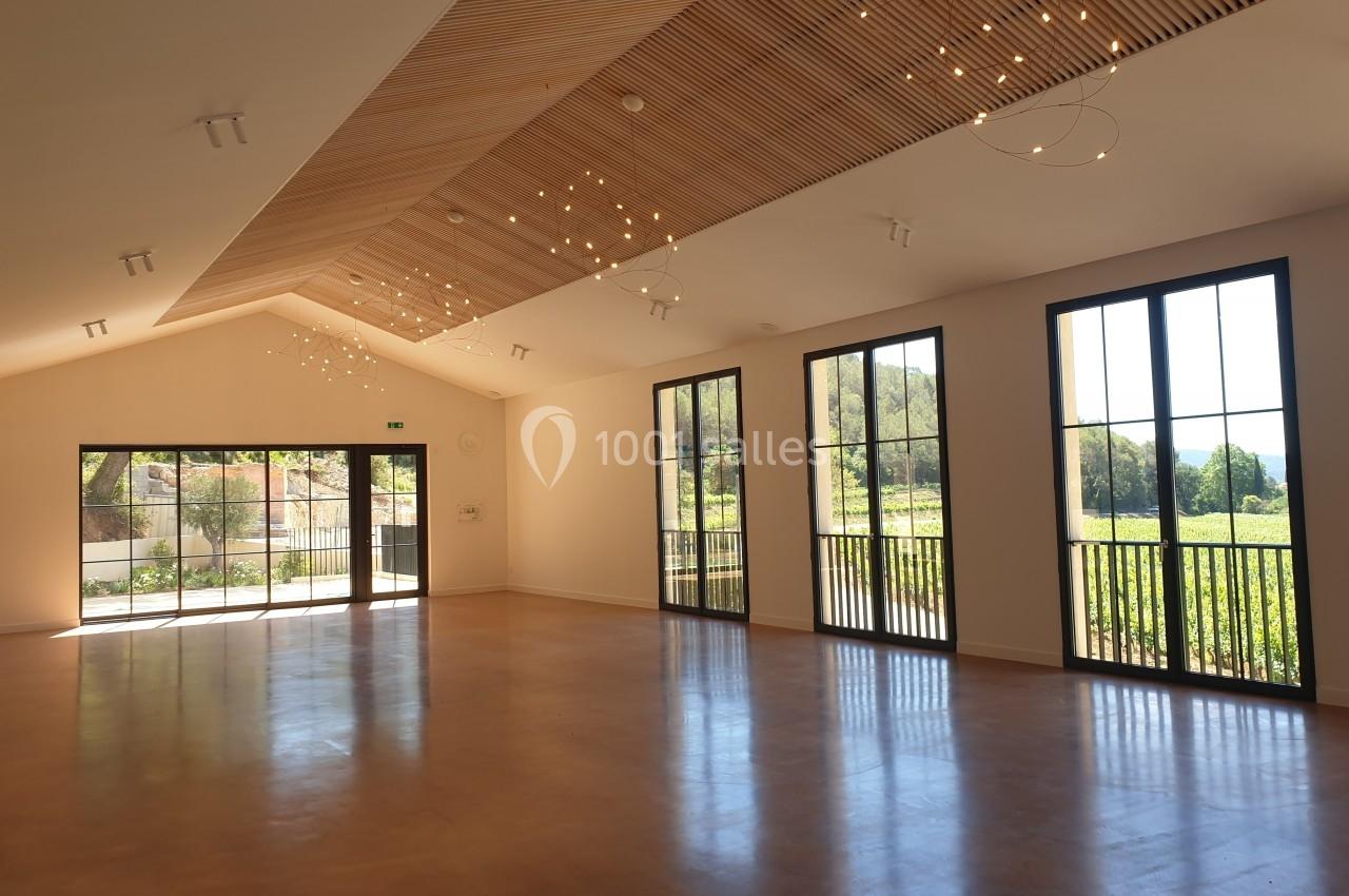 Salle lumineuse avec de grandes baies vitrées, un plafond en bois incliné et des luminaires suspendus.