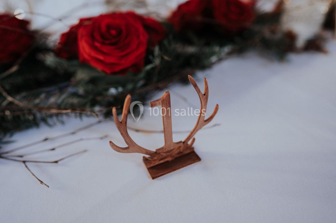 Centre de table avec un chiffre ’1’ en bois sur fond blanc, entouré de roses rouges et de branches de sapin.