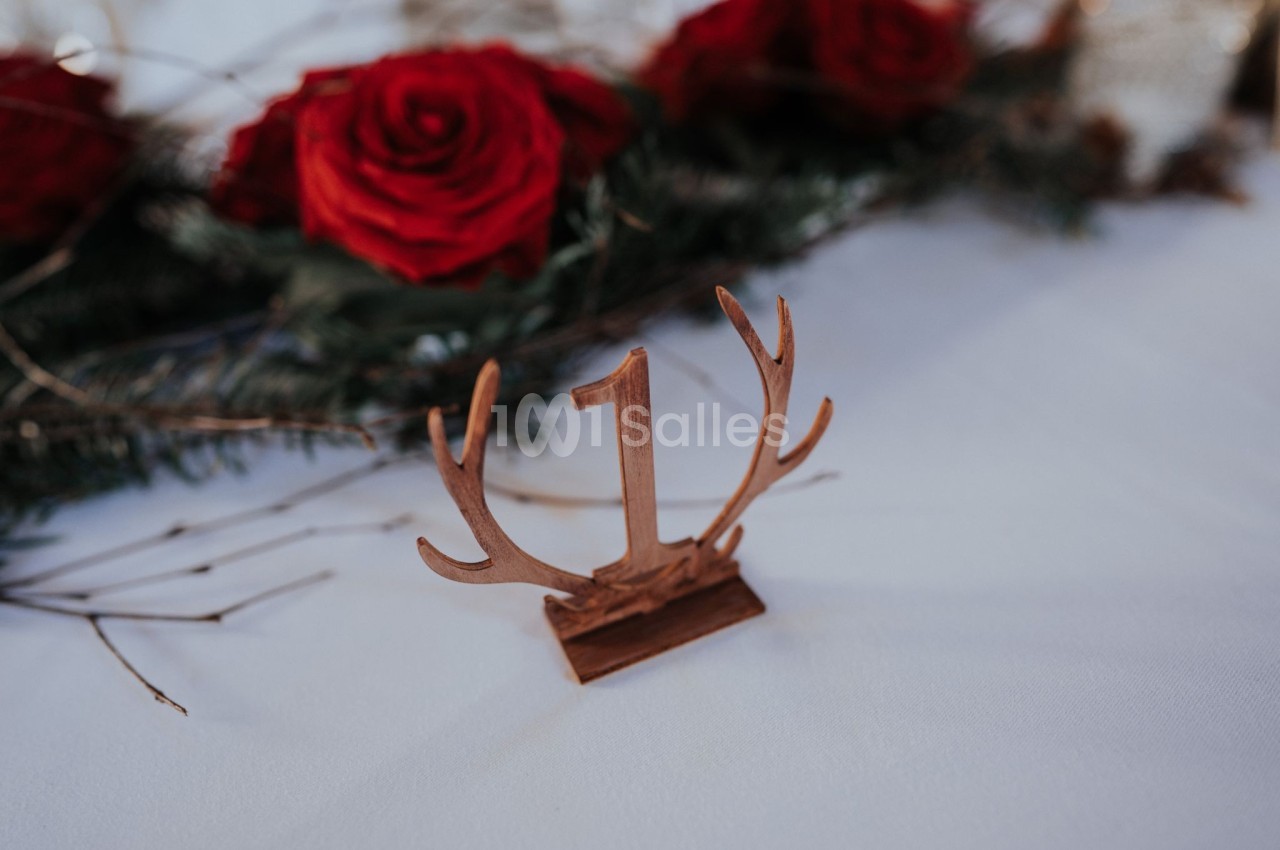 Centre de table avec un chiffre ’1’ en bois sur fond blanc, entouré de roses rouges et de branches de sapin.