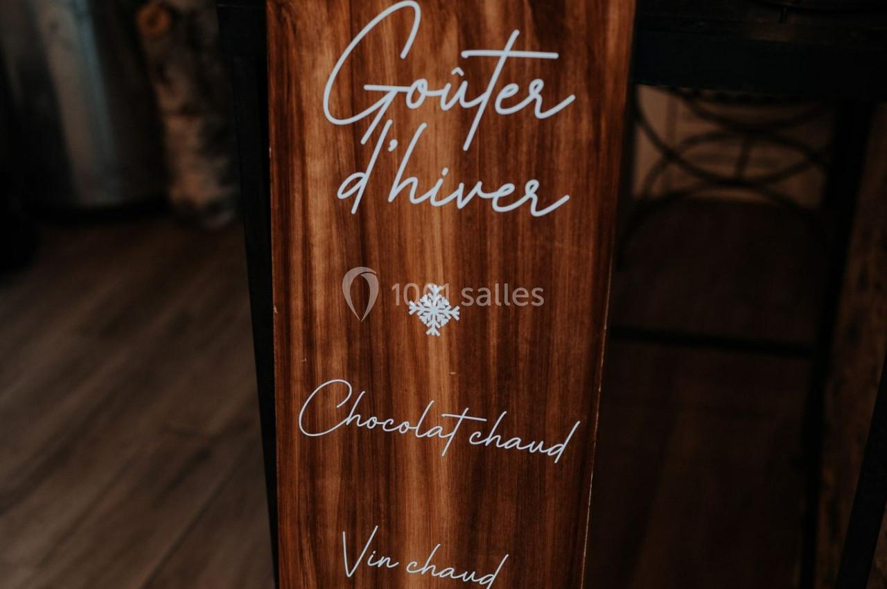 Panneau en bois avec l'inscription ’Goûter d'hiver’ et une liste incluant chocolat chaud et vin chaud.