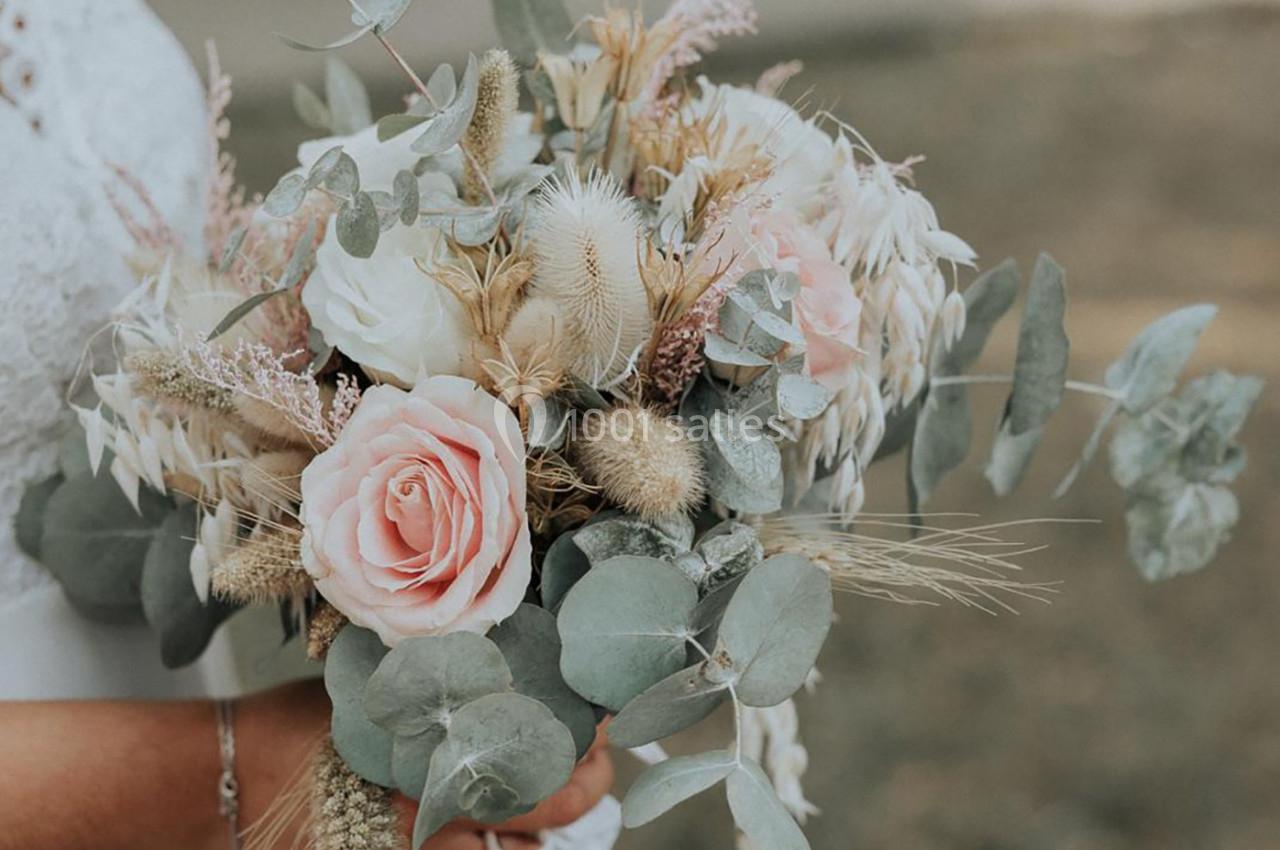 Bouquet de fleurs séchées et fraîches avec roses, eucalyptus et graminées, tenu par une personne en robe blanche.