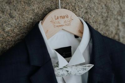 Costume de mariage bleu foncé avec chemise blanche et nœud papillon floral, suspendu sur un cintre gravé.