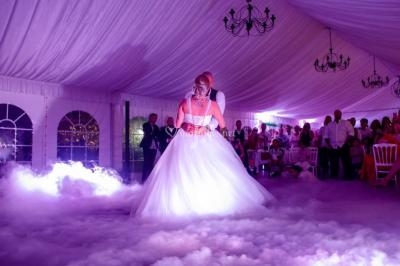 Un couple danse sous une tente éclairée, entouré de fumée et de convives assis.