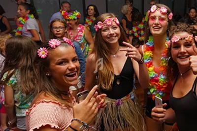 Des jeunes et des adultes participent à une fête sur le thème hawaïen, portant des colliers de fleurs et des tenues colorées.
