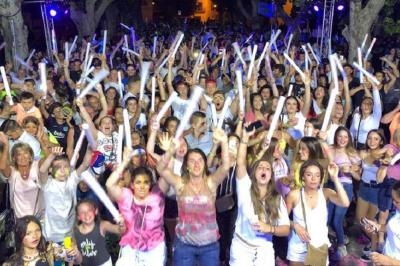Foule de personnes célébrant en soirée, agitant des bâtons lumineux dans une ambiance festive en extérieur.
