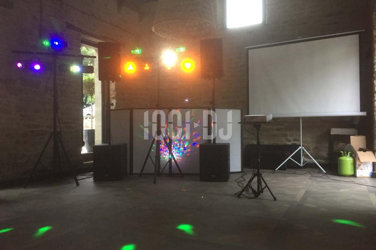 Équipement de sonorisation et éclairage coloré installé dans une salle en pierre avec un projecteur et un écran.