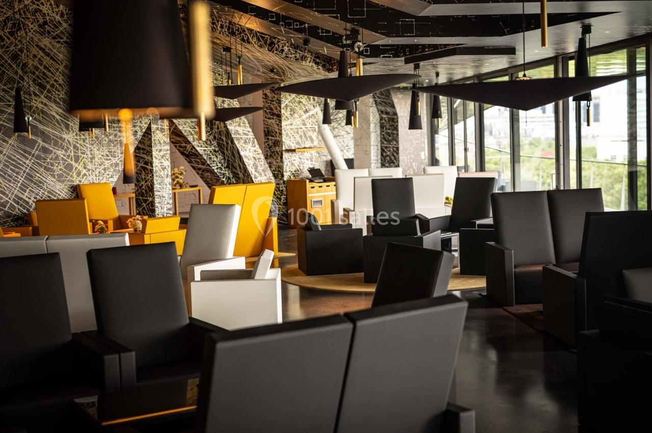 Espace intérieur moderne avec fauteuils noirs et jaunes, grandes fenêtres et décorations géométriques.