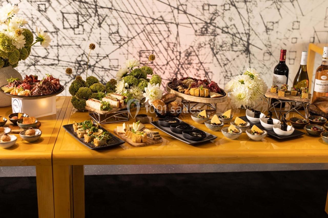 Buffet élégant avec une variété de plats, desserts, pains, fleurs décoratives et bouteilles de vin sur une table en bois.