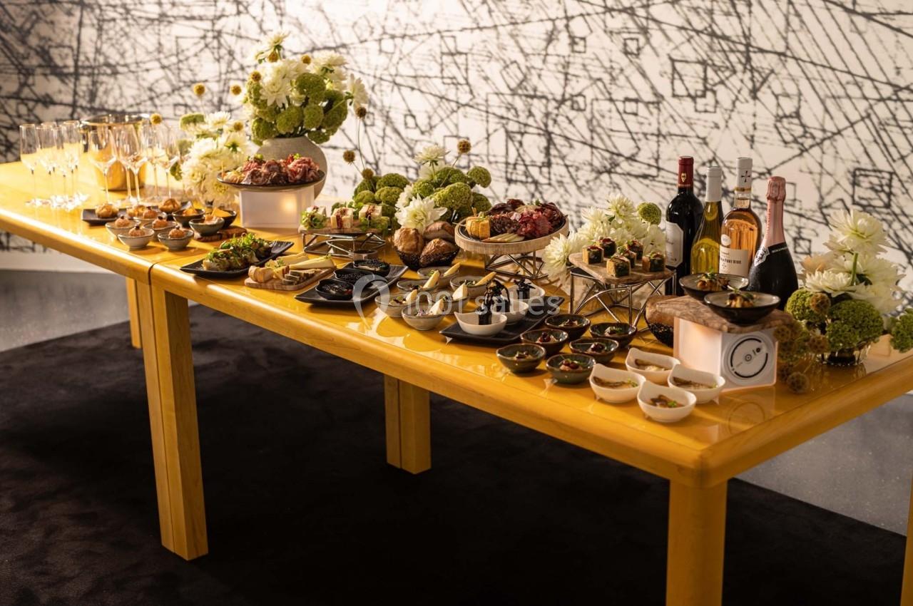 Table garnie de plats variés, fleurs blanches, bouteilles de vin et flûtes à champagne dans un cadre élégant.