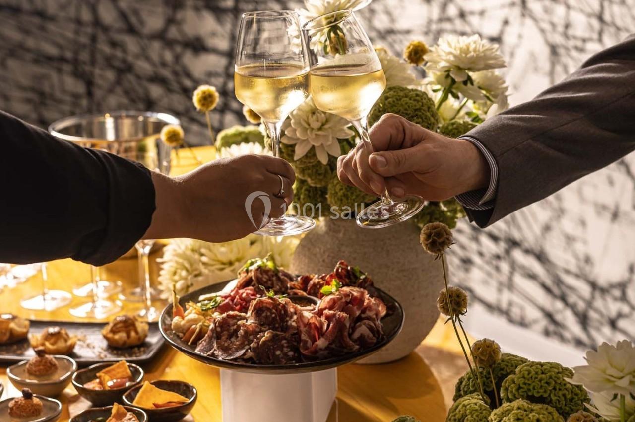Deux personnes trinquent avec des verres de vin blanc près d'une table garnie de plats et de fleurs décoratives.