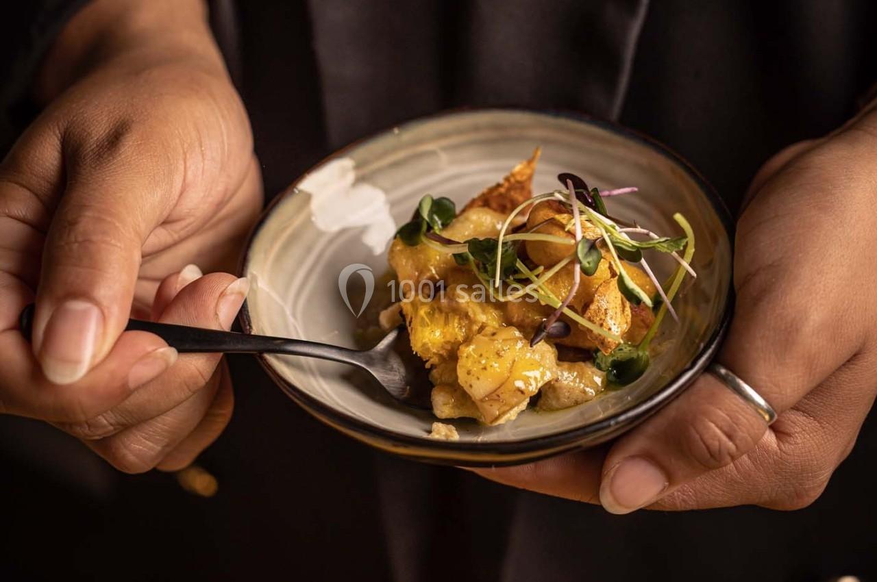 Une personne tient un petit bol contenant un plat garni de pousses fraîches, dégusté avec une fourchette.