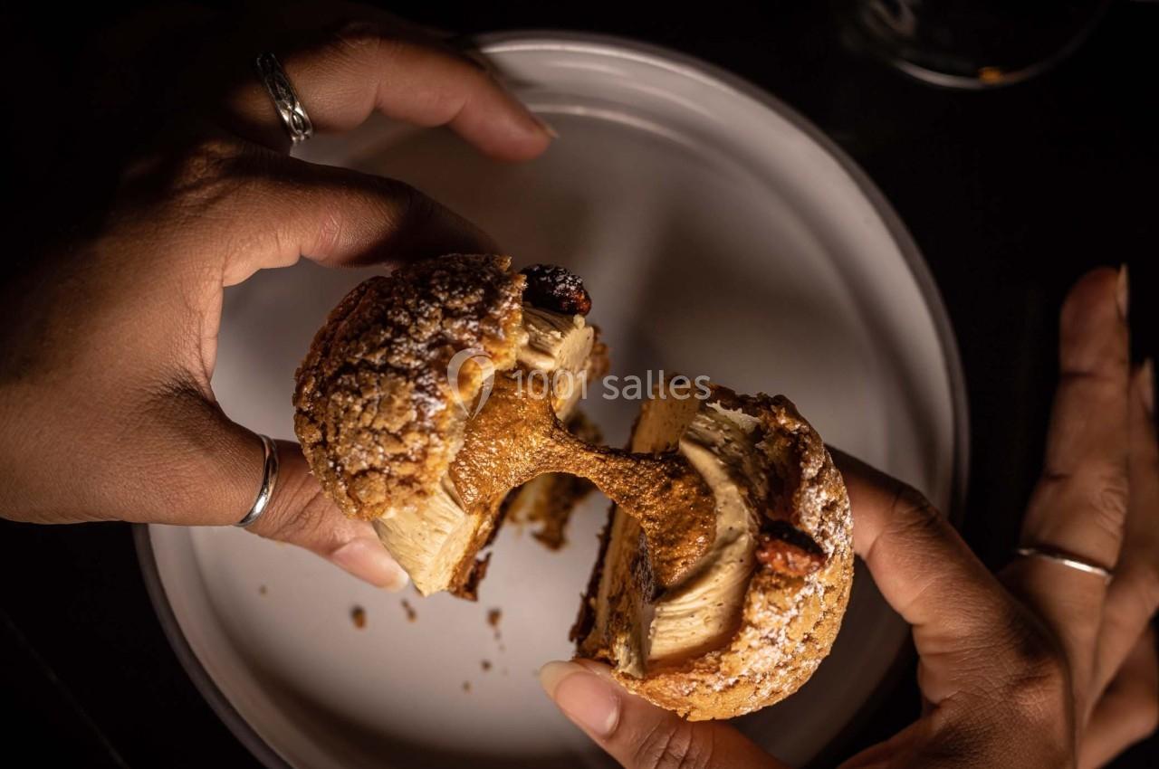 Deux mains séparent un chou pâtissier garni de crème caramel, posé sur une assiette blanche.