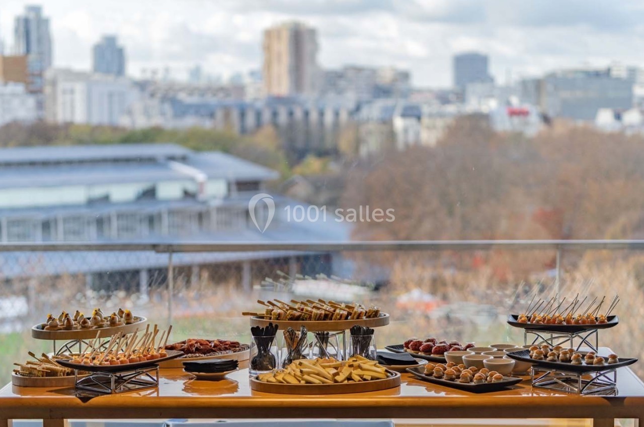 Buffet de bouchées apéritives variées disposées sur une table avec vue sur une ville en arrière-plan.