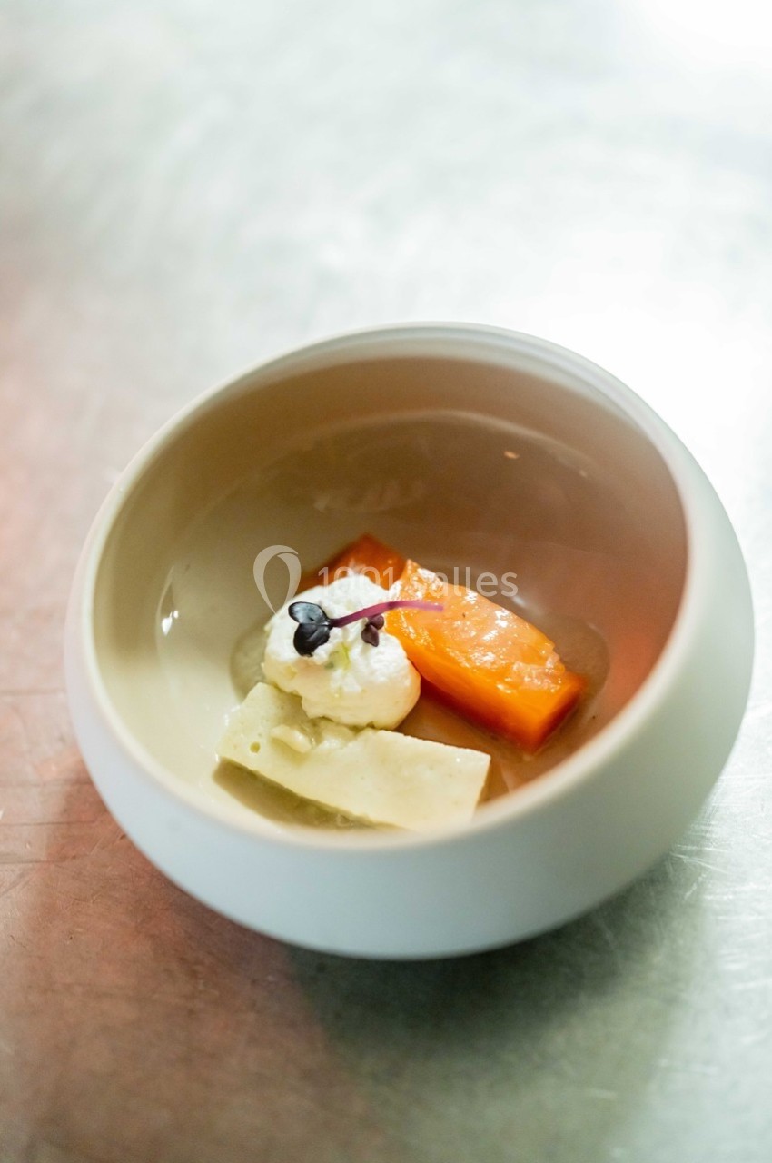 Assiette contenant un morceau de saumon, une quenelle de crème et une fine tranche de fromage, sur une table métallique.