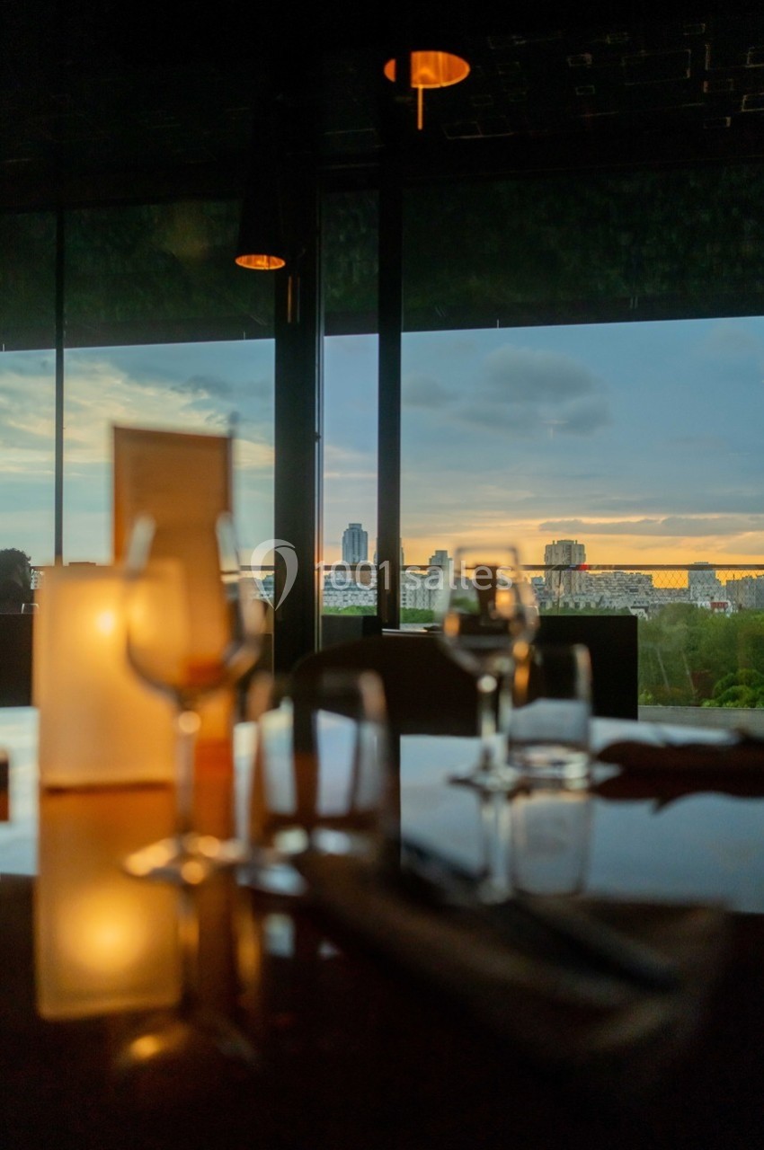 Vue d'une table dressée avec des verres et des bougies, donnant sur une grande baie vitrée au coucher du soleil.
