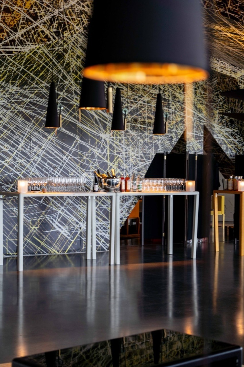 Salle moderne avec tables dressées, suspensions noires et mur décoré de motifs géométriques lumineux.