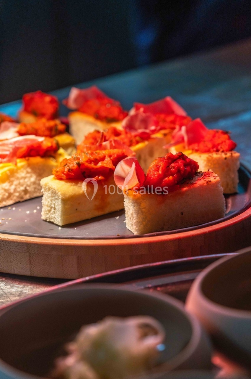 Assortiment de bouchées sur pain, garnies de légumes grillés et de charcuterie, présenté sur une assiette.