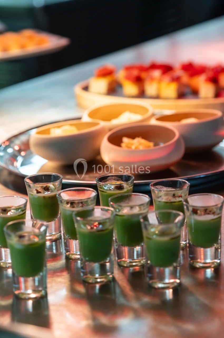 Petits verres de soupe verte et desserts variés disposés sur une table en métal.