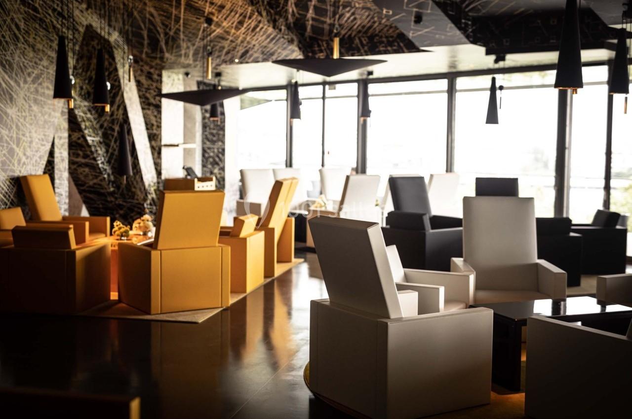 Espace intérieur moderne avec fauteuils design colorés, éclairage suspendu et grandes fenêtres laissant entrer la lumière.