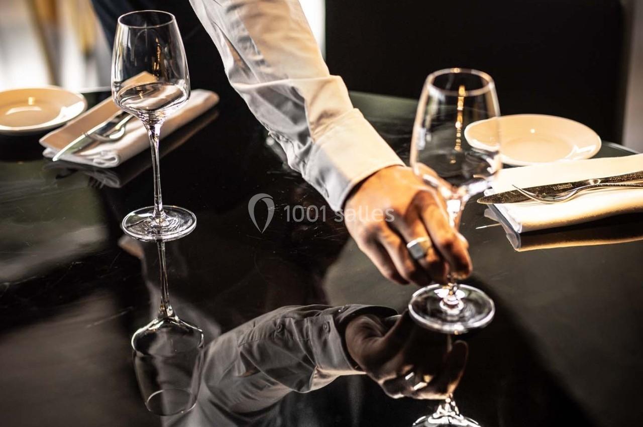 Un serveur ajuste un verre à pied sur une table noire dressée avec des assiettes et des couverts.