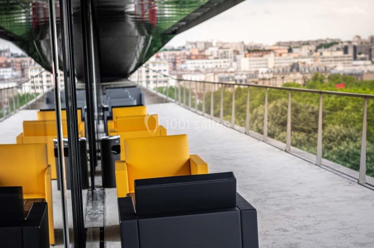Fauteuils jaunes et noirs alignés sur une terrasse moderne avec vue sur une ville et des espaces verts.