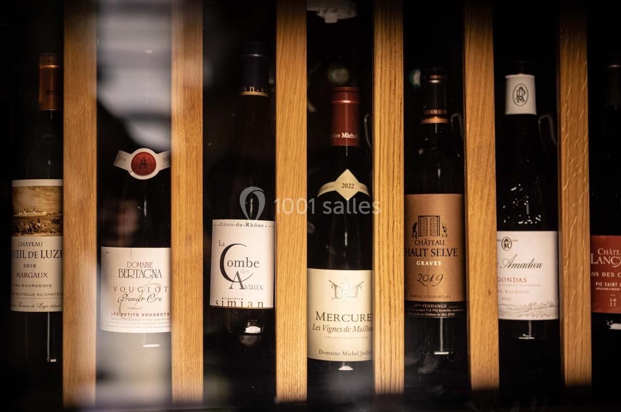 Bouteilles de vin rouge et blanc alignées dans une étagère en bois, étiquettes visibles sous un éclairage tamisé.